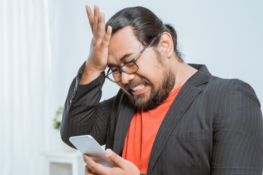 Man looking at phone with frustrated expression while looking at his smartphone and hitting his palm on his forehead.